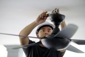 An Asian man is changing ceiling fan at residence.